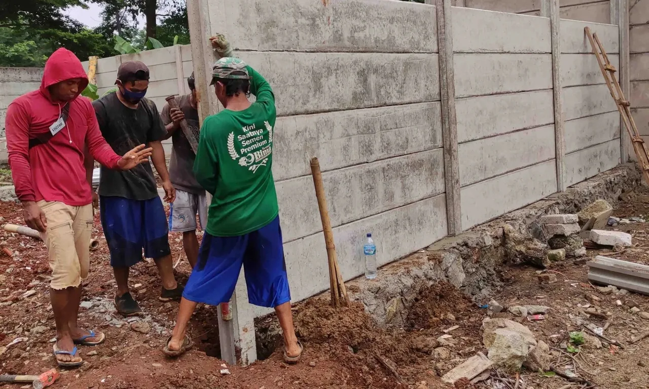 Pemasangan panel pagar beton pracetak ke kolom, dikerjakan empat tukang
