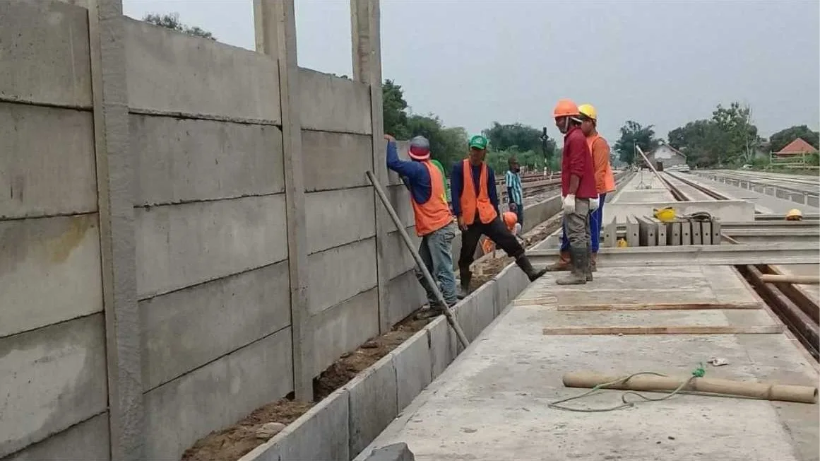 Panel pagar beton pracetak terpasang di proyek jalan, pekerja ber-APD lengkap