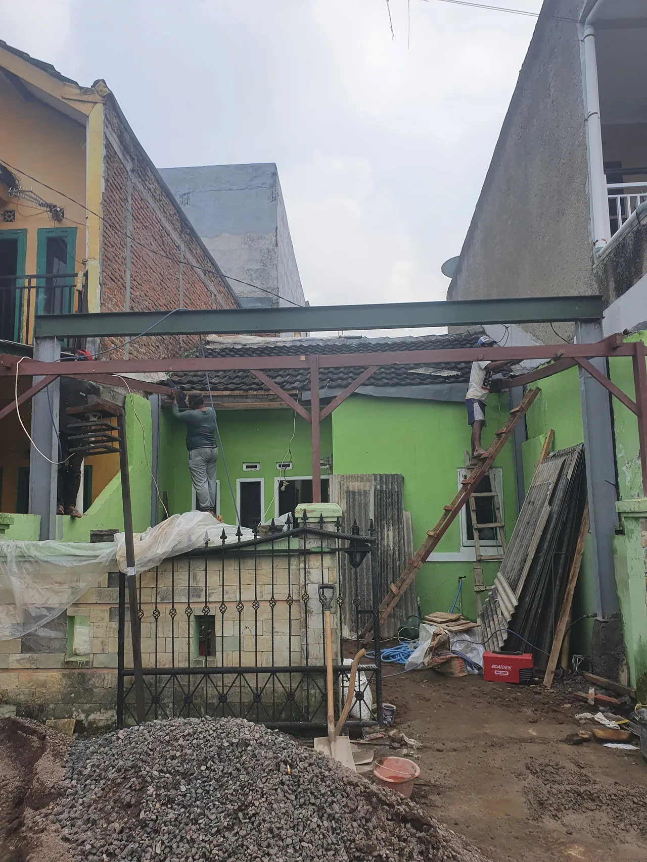 Rangka baja lantai dua dipasang di atas rumah lama, dua tukang bekerja di ketinggian